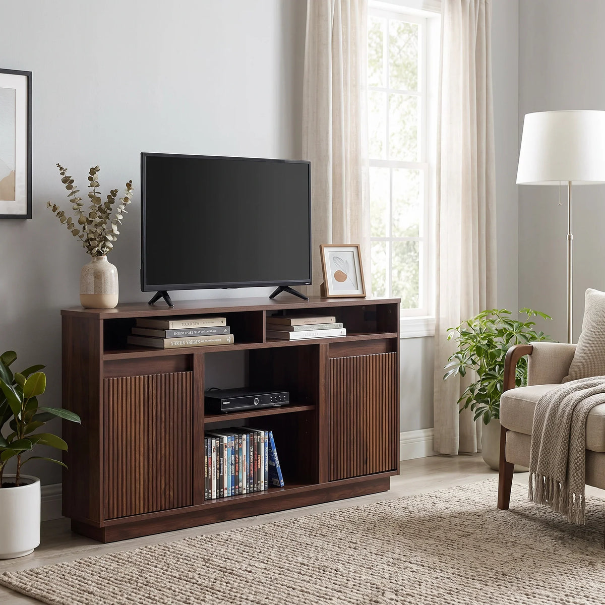 Dark wood media console with TV, books, and decorative items in a bright living room.