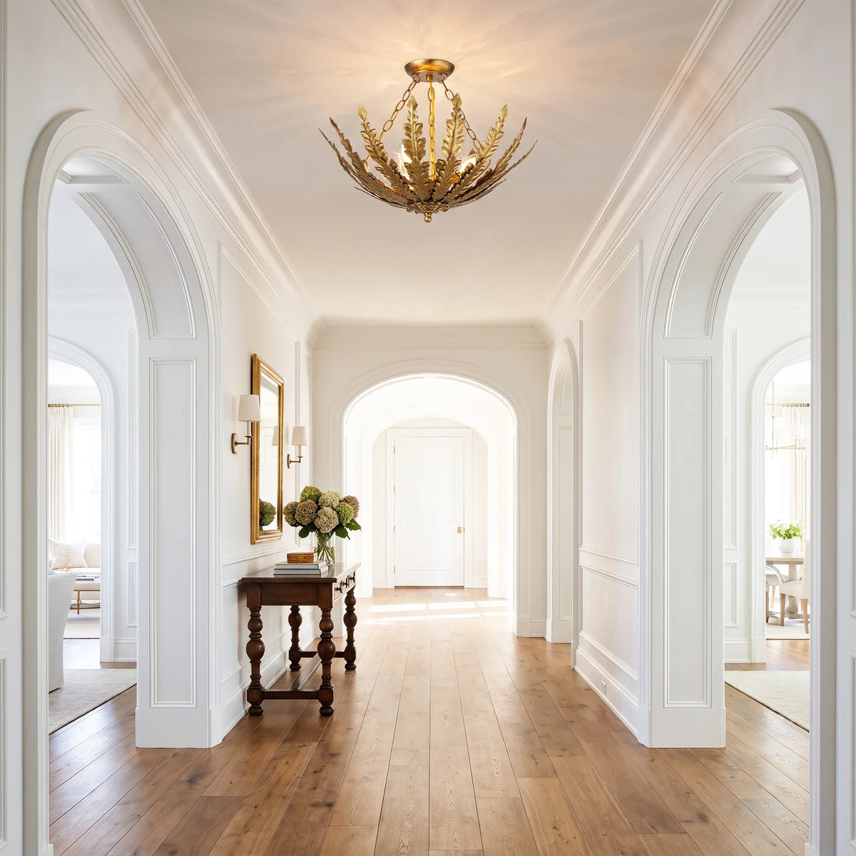 Gold leaf-shaped chandelier hanging in a white classical hallway
