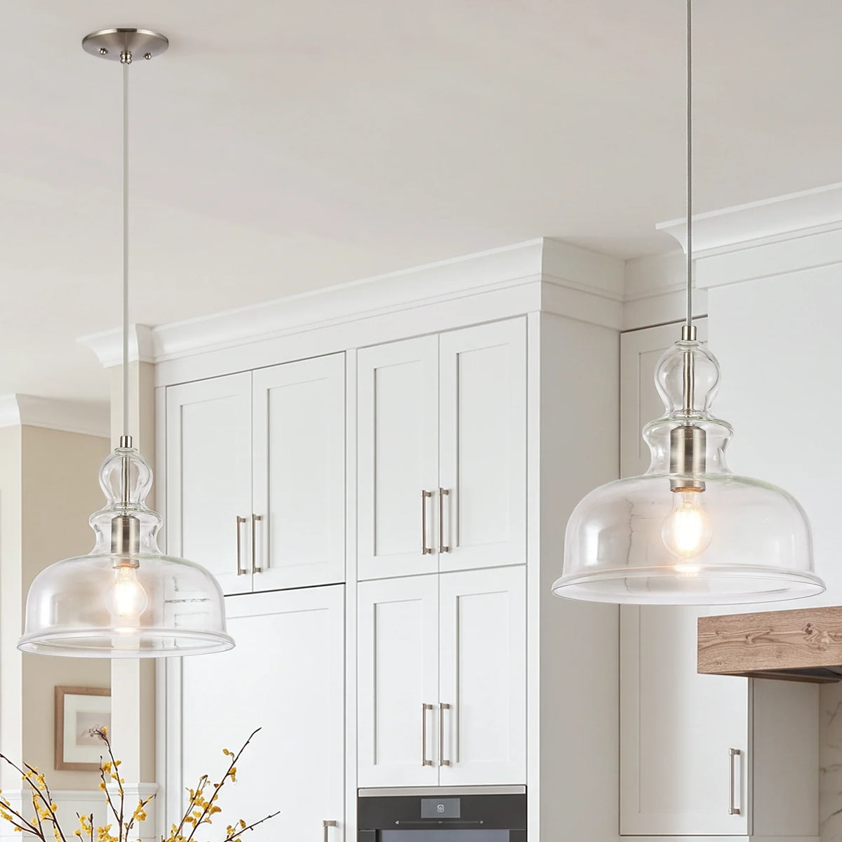 Two clear glass bell-shaped pendant lights hanging in a white modern kitchen