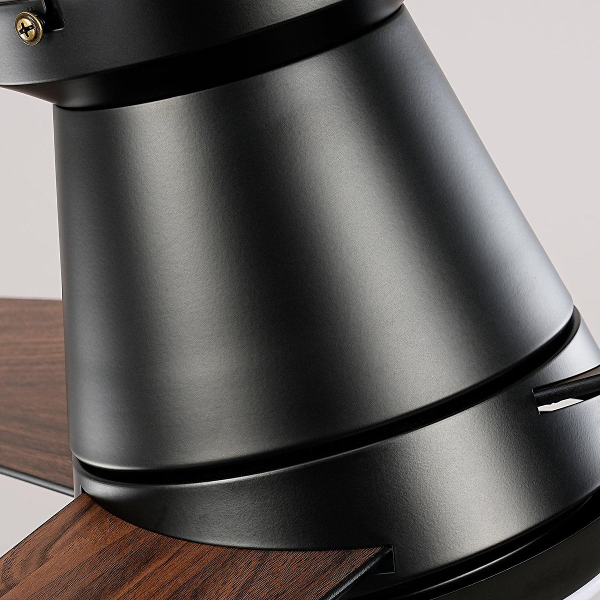 Close-up of the black matte finish motor housing and wooden blade of a ceiling fan.